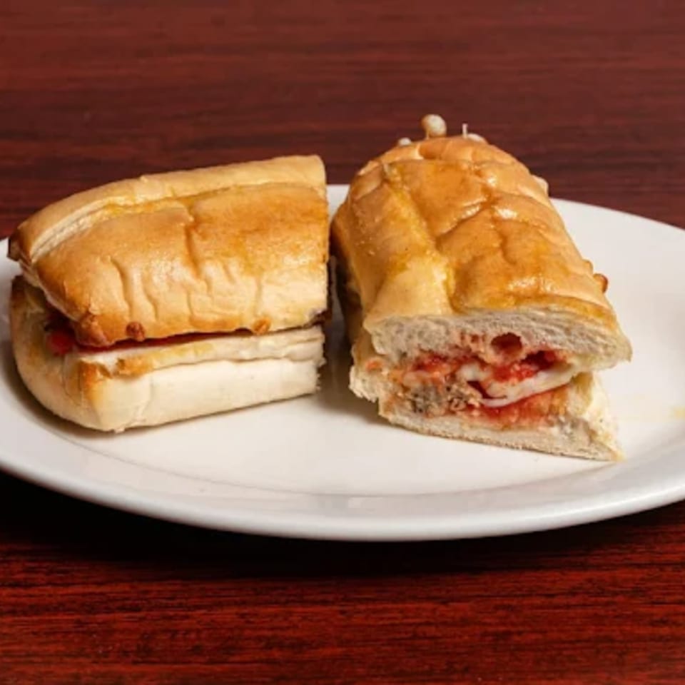 Two halves of a meatball sub sandwich with marinara sauce and melted cheese on a white plate.